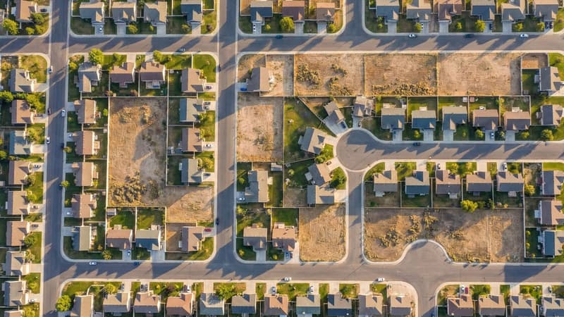 Aerial view of a suburban housing development with neat rows of homes and empty lots, representing constrained housing supply and stalled spring market conditions