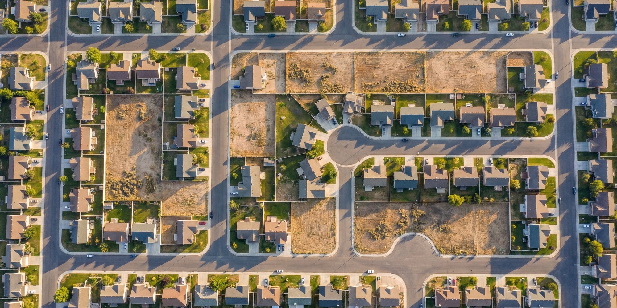 Aerial view of a suburban housing development with neat rows of homes and empty lots, representing constrained housing supply and stalled spring market conditions