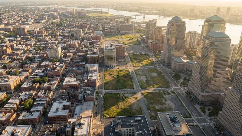 Aerial view of an American city grid showing contrasting vacant parcels and developed blocks near the financial district at golden hour, illustrating the economics of idle land value