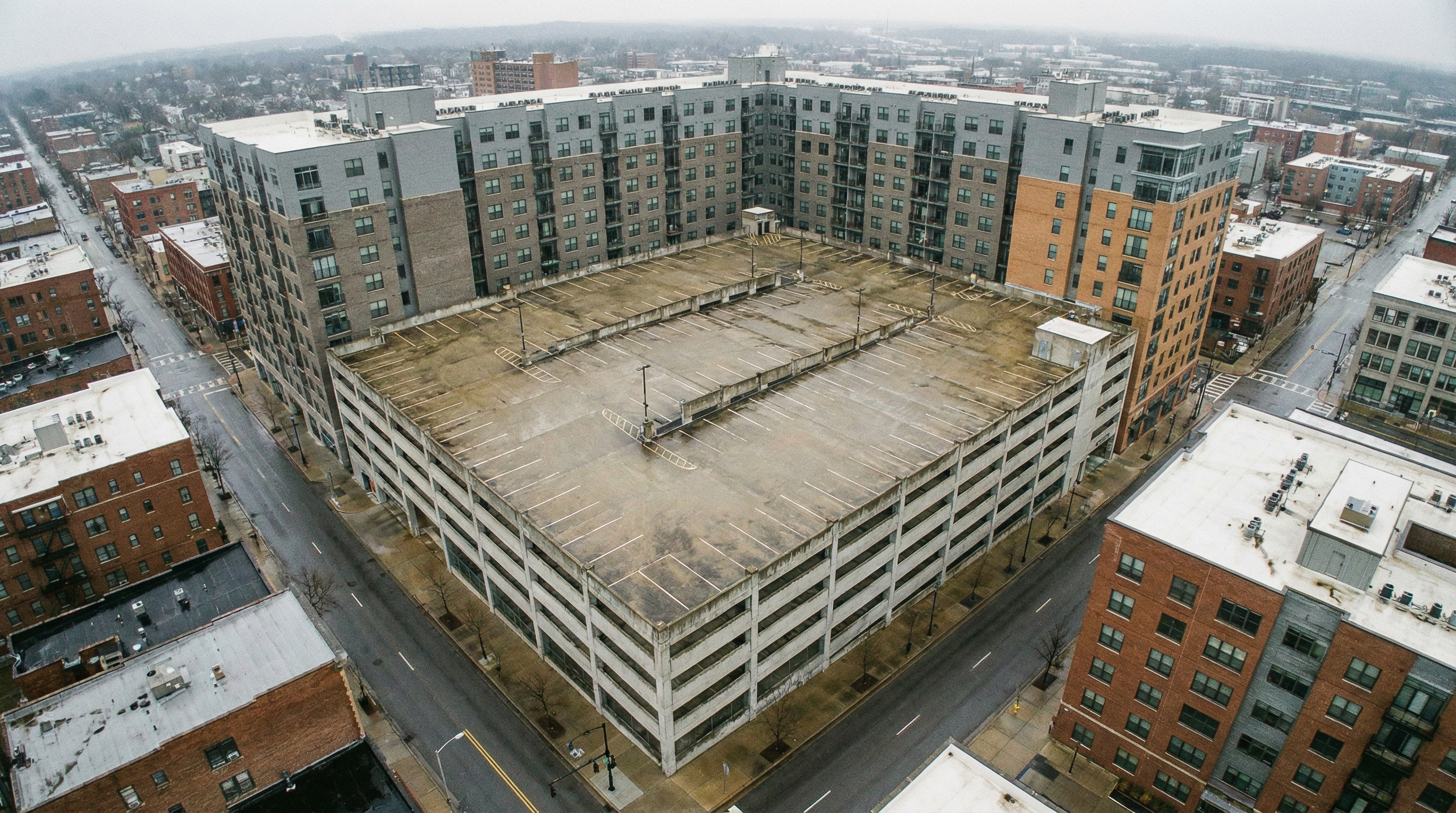 Multi-story concrete parking garage adjacent to urban apartment buildings, showing repeating rows of empty parking spaces across elevated deck levels