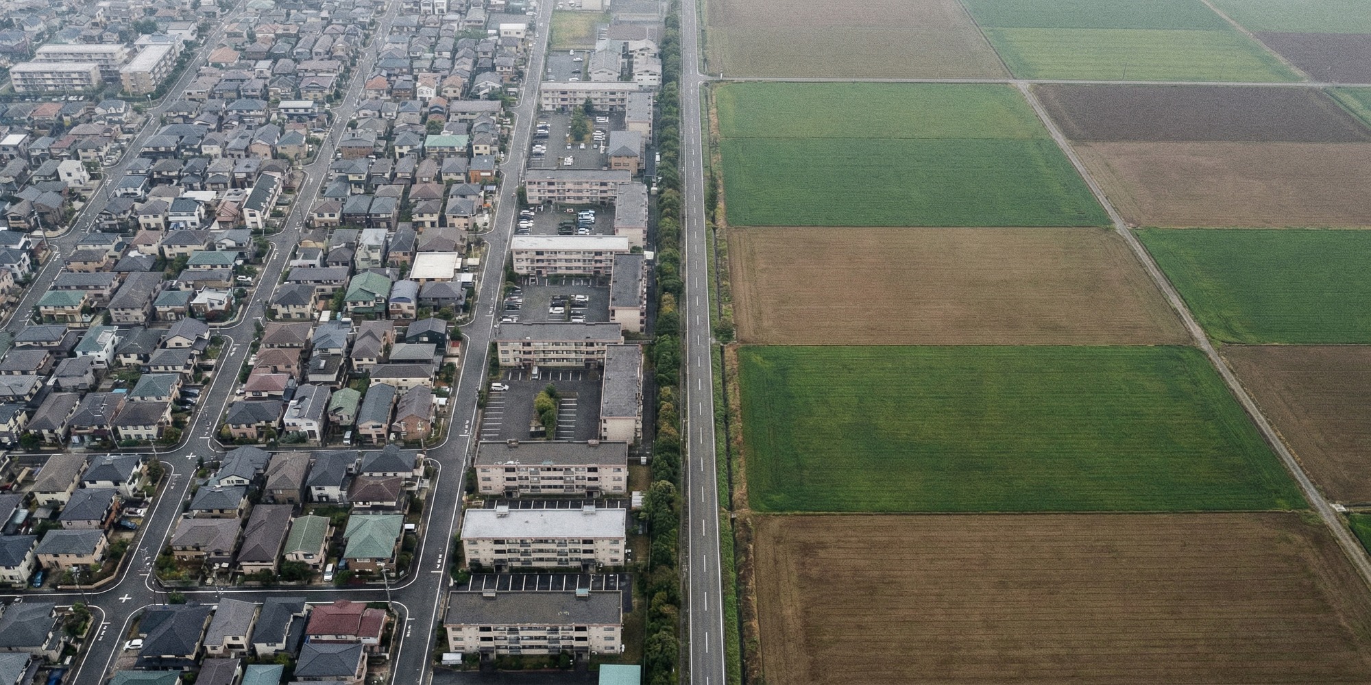 Aerial view of a dense urban district with compact housing blocks meeting open farmland at a sharp boundary line
