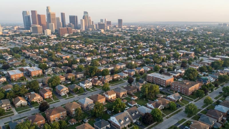 Aerial view of a dense residential neighborhood with single-family homes stretching to a distant financial district skyline