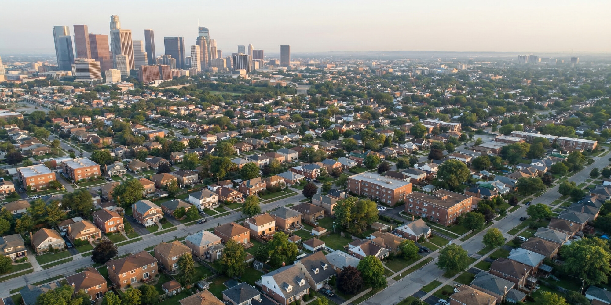 Aerial view of a dense residential neighborhood with single-family homes stretching to a distant financial district skyline